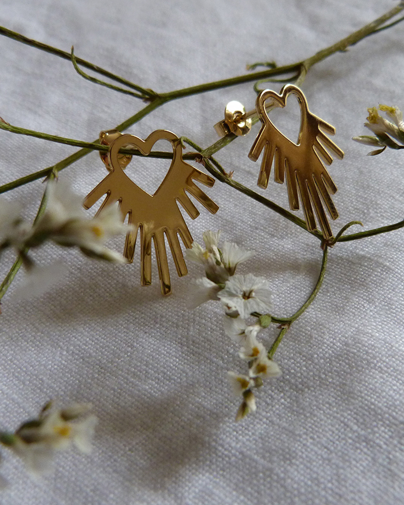 Puces d'oreilles dorées en forme de cœur rayonnant posées sur une branche de fleurs séchées, sur du lin blanc
