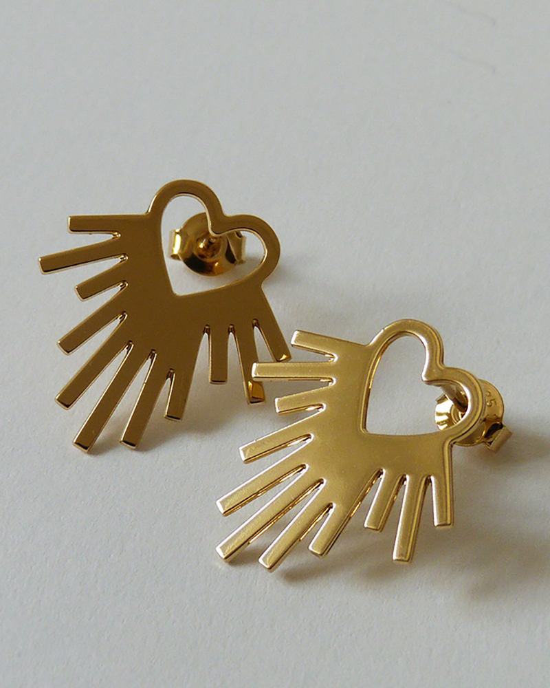 Paire de boucles d'oreilles dorées, cœur ajouré entouré de rayons, vue de près sur fond gris clair