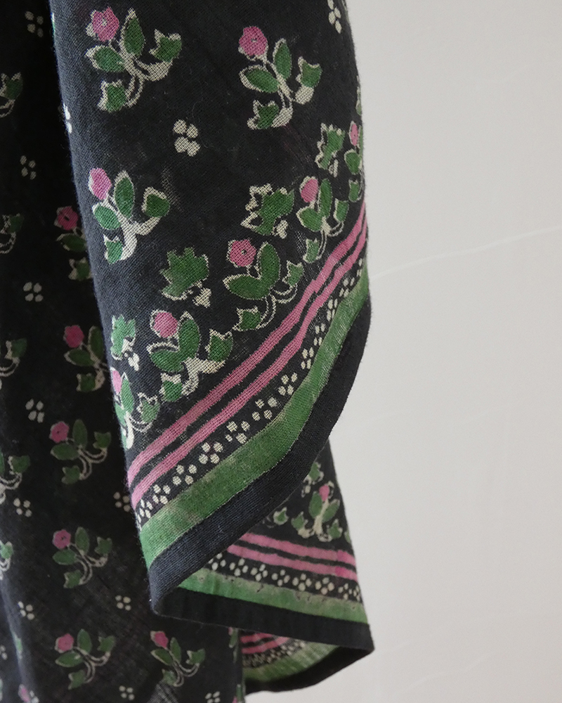 Coin d'un foulard carré en gaze de coton noir, bouquets fleuris vert et fuchsia et bordure rayée